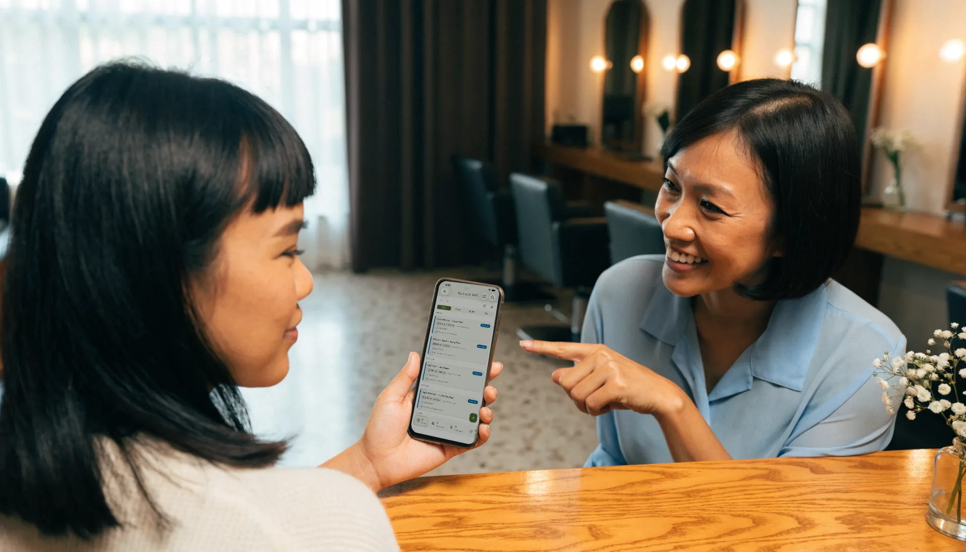 At the front desk the receptionist shows a client the day’s appointment schedule on Fuze Store on her phone as they pick a time.
