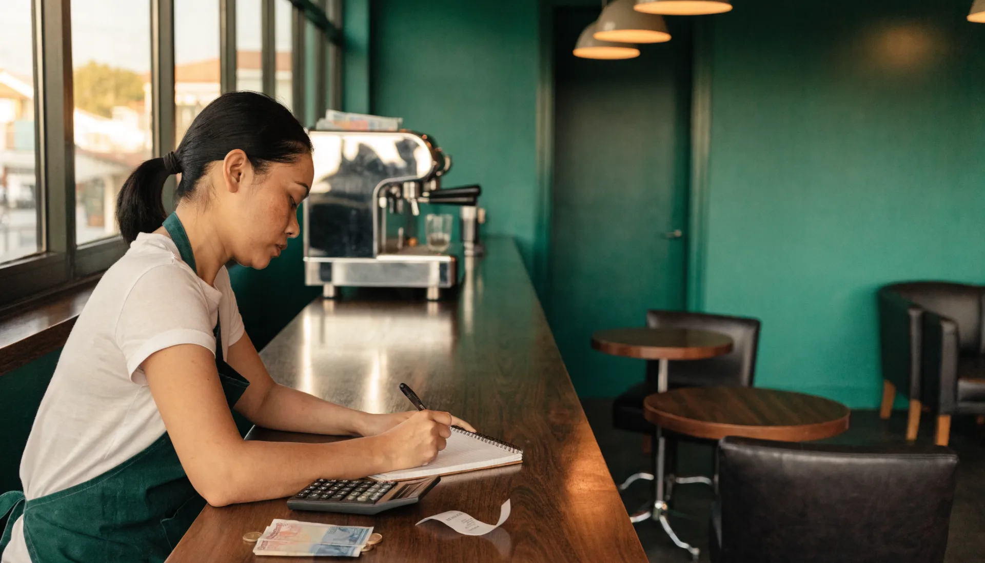 Closing time, chairs up — the owner works out the day in a notebook with a calculator, peso bills, and a curl of receipt paper.