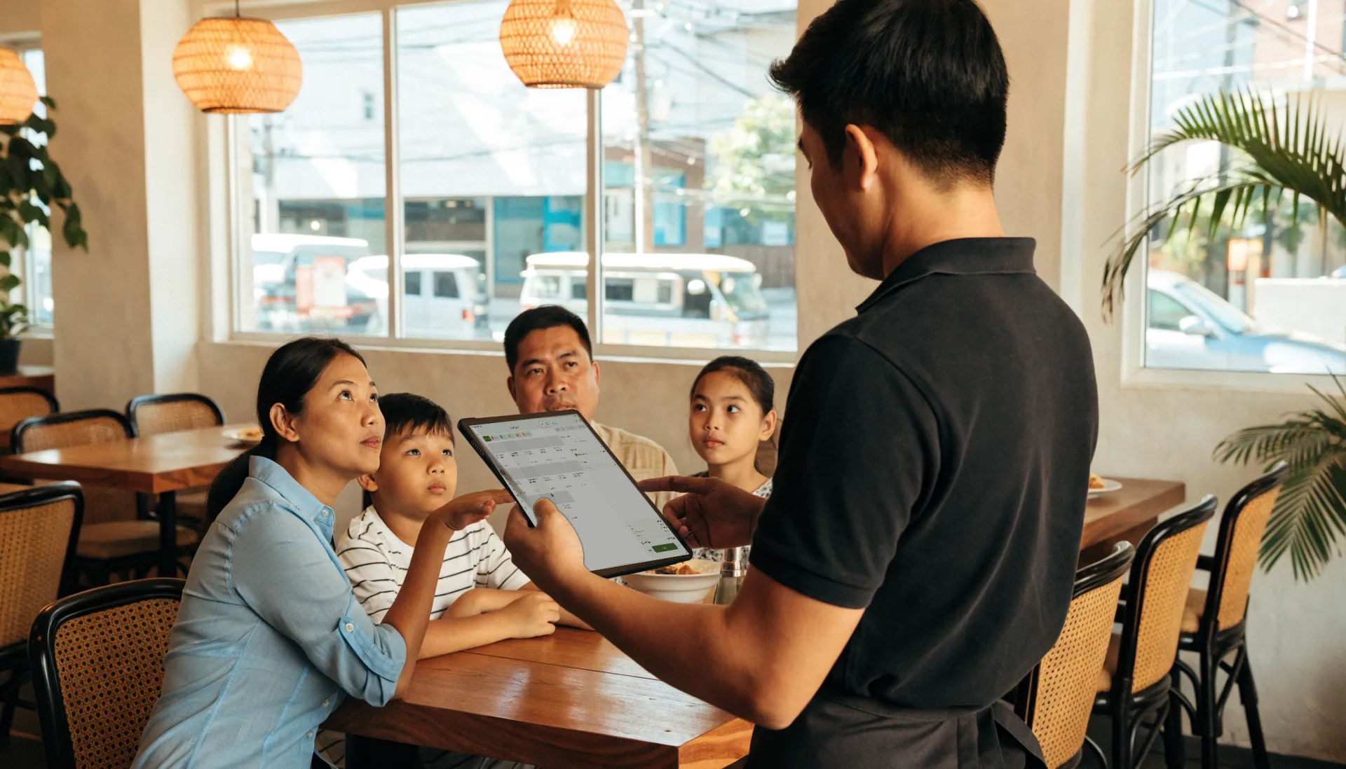 A server at a family table taps their order into the Fuze Store register on his tablet while the mother points out a dish.